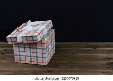 Gift box upholstered in checkered material with a white bow on a dark wooden table. Close up. Copy space. - Powered by Shutterstock