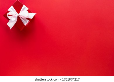 Gift Box With White Bow On Red Background, Top View With Copy Space.