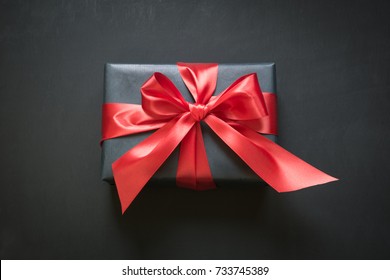 Gift Box Wrapped In Black Paper With Red Ribbon On Black Surface. Top View.