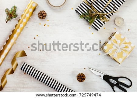 Gift box wrapped in black and white striped paper, a crate full of pine cones and christmas toys and wrapping materials on a white wood old background. Christmas presents preparation.