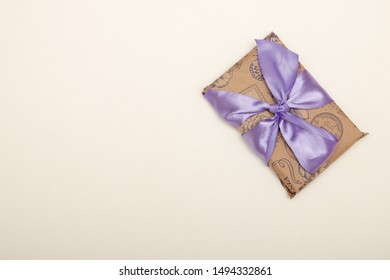 Gift Box Wrapped In Brown Paper With A Purple Satin Bow On A White Background Copy Space Top View