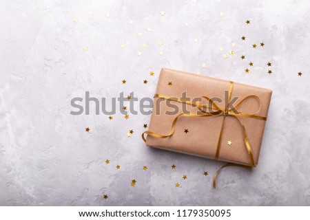 Gift box wrapped in craft paper with gold ribbon and stars on grey stone