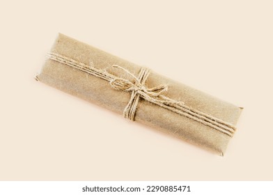 gift box wrapped in kraft paper and tied with twine on a beige background. Top view. Vintage gift box made of brown eco-paper, tied with a rope.