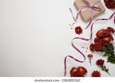 Gift box wrapped in kraft paper, ribbon and red chrysanthemum flowers on white background.  Festive arrangement. Flat lay. Copy space for text. - Powered by Shutterstock