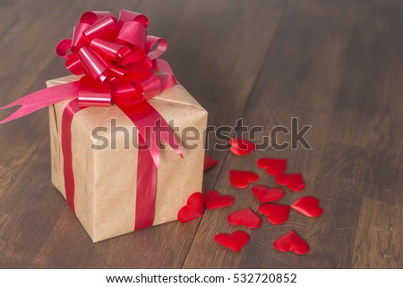 Gift box wrapped in recycled paper with red ribbon bow on a background of red hearts.