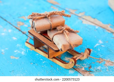 Gift Boxes. Close-up Wrapped Craft Vintage Gift Box Lying Wooden Toy Sled On Blue Old Wooden Background. Present Box In Craft Paper. Holiday Concept. Xmas, Christmas Backdrop. Many Eco Presents.