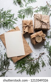 Gift Boxes On White Table And Fir Branches. Box With Ribbon Bow Present On Holiday Wrapped Paper. Minimalistic Christmas Gifts And Card Mockup