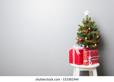 Gift Boxes And Small Decorated Christmas Tree On Gray Wall Background