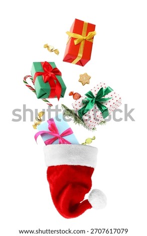 Gift boxes and sweets falling into Santa hat on white background