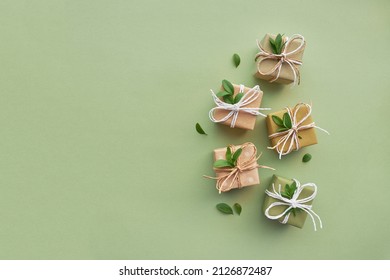 Gift Boxes Wrapped In Kraft Paper And Decorated With Leaves On A Green Background. Eco Friendly Present Concept.