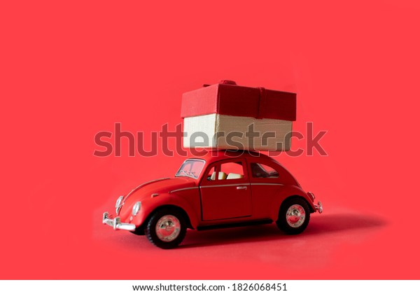 Gift by car. Red toy retro car delivering a gift on\
a red-orange background. Postcard for New Year, Christmas,\
Valentine\'s Day. Delivery of gifts. March 8. Kiev, Ukraine\
September 19, 2020