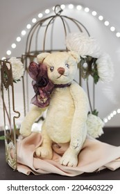 Gift Card Image Of Standing Plush Handmade Teddy Bear Standing At Bird Cage Decorated With White Flowers And Bokeh Lights On Background. Vintage Style Toy Concept. Childhood Nostalgia