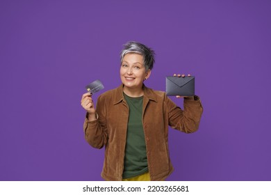 Gift Card In Mature Woman Hand With Fancy Dark Envelope. Happy Mature Woman Got Her New Bank Debit, Credit Card, Wearing Casual Isolated On Purple Background. Banking, Financial Concept. 