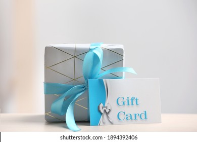 Gift Card And Present On Table Against Blurred Background