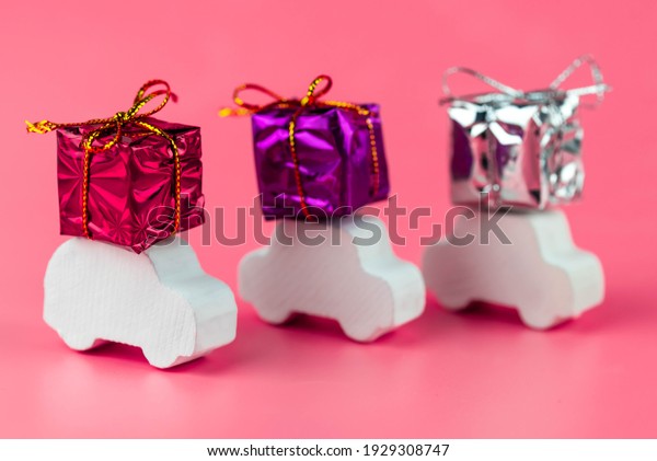 Gift delivery concept. Toy car delivers gift box\
on pink background. February 14 postcard, Valentine\'s Day,\
Christmas, New year, \
 March 8, international women\'s day.\
Minimalism style.