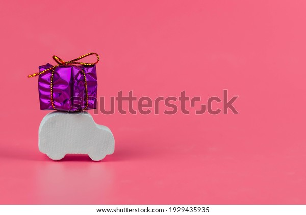 Gift delivery concept. Toy car delivers gift box
on pink background. February 14 postcard, Valentine's Day,
Christmas, New year, 
 March 8, international women's day.
Minimalism style.