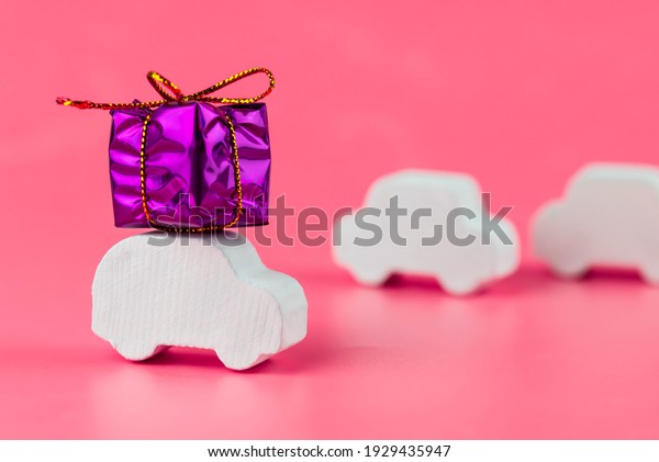 Gift delivery concept. Toy car delivers gift box\
on pink background. February 14 postcard, Valentine\'s Day,\
Christmas, New year, \
 March 8, international women\'s day.\
Minimalism style.