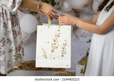 A gift from godparents for the first holy communion. A woman giving the girl a First Communion gift. First Communion gifts in decorative bags. - Shutterstock ID 2149403215