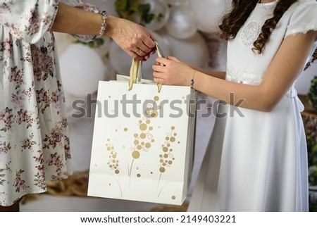 A gift from godparents for the first holy communion. A woman giving the girl a First Communion gift. First Communion gifts in decorative bags.