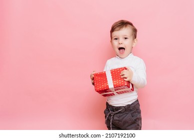 Gift In Hands Boy. Happy Baby Boy With Gift Box In Hands Isolated On Pink Background.