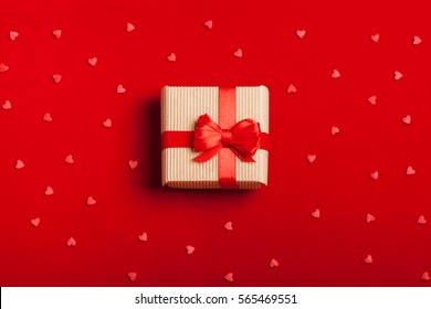 A gift in kraft box with a red bow on a red background with hearts. Surprise your loved one. The concept of the day of St. Valentine's, weddings, birthday, New Year, Christmas and other holidays