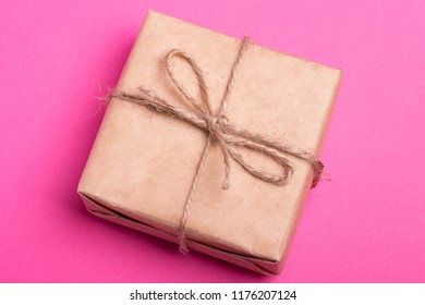 А Gift In A Kraft Wrapper, Tied With String On A Pink Yellow Background. A Corporate Present.