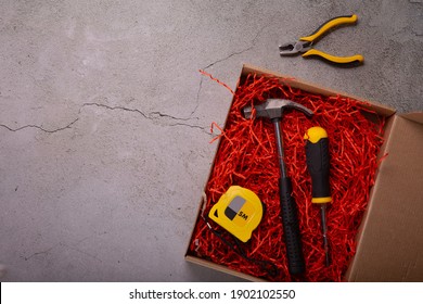 A Gift For A Man For The Holiday. Tool Box: Hammer, Screwdriver, Tape Measure, Pliers And Dried Fish On A Gray Background. View From Above