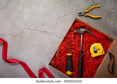 A Gift For A Man For The Holiday. Tool Box: Hammer, Screwdriver, Tape Measure, Pliers And Dried Fish On A Gray Background. View From Above