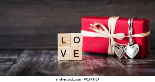 gift in red box  pendant in the shape heart silver chain   the word love  lined and square wooden blocks  dark wooden background