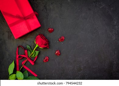 Gift for Valentine's day. Red rose, gift box, red hearts signs on black background top view copy space