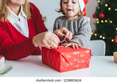 Gift wrapping. Little girl helps her grandmother to wrap Christmas present - Powered by Shutterstock