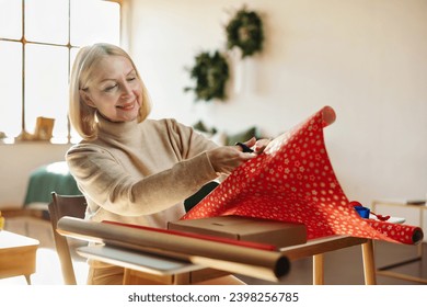 Gift wrapping in red packaging paper. Mature woman wrapping gift box. Packaging and preparation of gifts for the celebration of Christmas. - Powered by Shutterstock