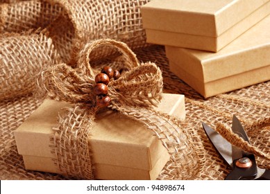 Gift wrapping still life with small brown boxes being decorated with eco friendly burlap ribbon and tiny wooden beads.  Macro with shallow dof. - Powered by Shutterstock