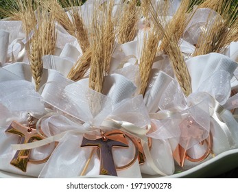 Gifts Or Favors For The First Or Holy Communion. Small Bags Of White Fabric With Ear Of Wheat And Tau Christian Cross. Religious Symbol