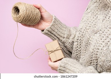 Gifts made of Kraft paper, a coil of rope in women's hands on a pink background, close-up. Handmade gifts concept. Modern trend, natural gift wrapping with your own hands. Holiday background. - Powered by Shutterstock