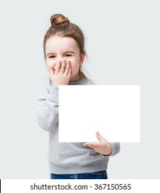 Giggles Happy Kid Girl Closes Face With Her Hand. Confused Little Girl Holding A Poster For Your Information. Gray Background Do Not Speak