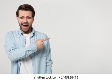 Giggling millennial man wearing blue shirt points finger at empty copy space for text posing isolated on grey studio background show laughing at something shameful awkward and strange, mockery concept - Powered by Shutterstock