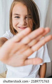 Giggling Tween Girl Blocking Camera With Her Hand, Smiling With Her Baby Teeth. Against A White Curtain.