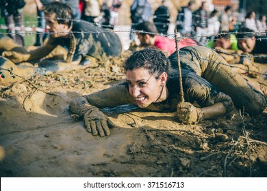 GIJON, SPAIN - JANUARY 31, 2016: Farinato Race Event, A Extreme Obstacle Race, Celebrated In Gijon, Spain, On January 31, 2016. Portrait Of Woman Crawling Under A Barbed Wire In A Test Of The Race.