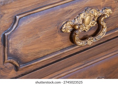 Gilded brass pull handle decorating an old brown wooden furniture drawer