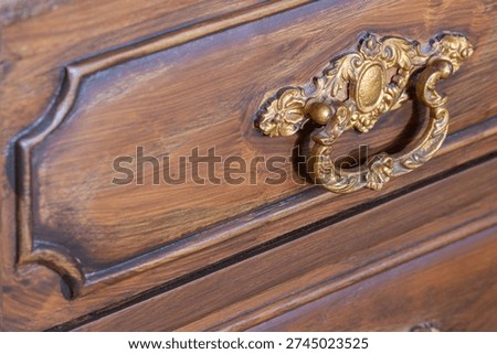 Gilded brass pull handle decorating an old brown wooden furniture drawer