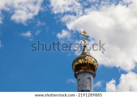 Gilded dome with a cross of an Orthodox church against a blue sky with white clouds