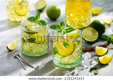 Gin fizz cocktail with lime and mint lemonade, ice tea in glasses and jug. Close up. 
