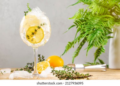 Gin tonic alcoholic cocktail drink with dry gin, bitter tonic, lemon juice, thyme and ice, bar tools. Wooden table background with copy space