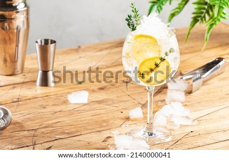 Gin tonic alcoholic cocktail drink with dry gin, bitter tonic, lemon juice, thyme and ice, bar tools. Wooden table background with copy space
