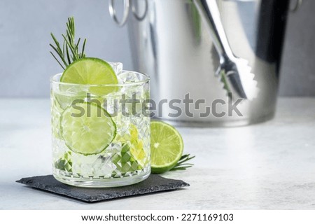 Gin tonic classic cocktail drink with dry gin, bitter tonic, lime and ice. Gray table background 