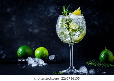 Gin tonic cocktail with dry gin, rosemary, tonic, lime and ice cubes in wine glass. Black bar counter background, bar tools, copy space - Powered by Shutterstock