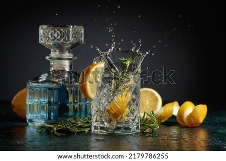Gin tonic cocktail with lemon and rosemary. Slice of lemon fall in glass with a cocktail.