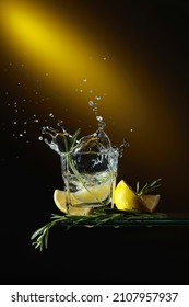 Gin And Tonic Cocktail With Lemon Slices And Rosemary Sprigs. A Slice Of Lemon Falls Into The Glass Creating A Beautiful Splash.