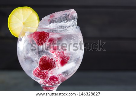 Gin tonic cocktail with raspberry lima slice and ice macro closeup on black